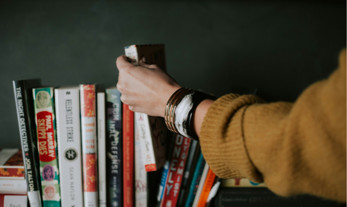 Womens hand reaching out to grab books from shelf