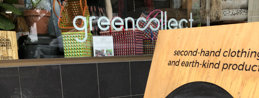 A wooden A-frame sign with a black chalkboard circle displaying the handwritten message "WORKING TOWARDS A CIRCULAR ECONOMY," placed on a sidewalk near a black tiled wall.