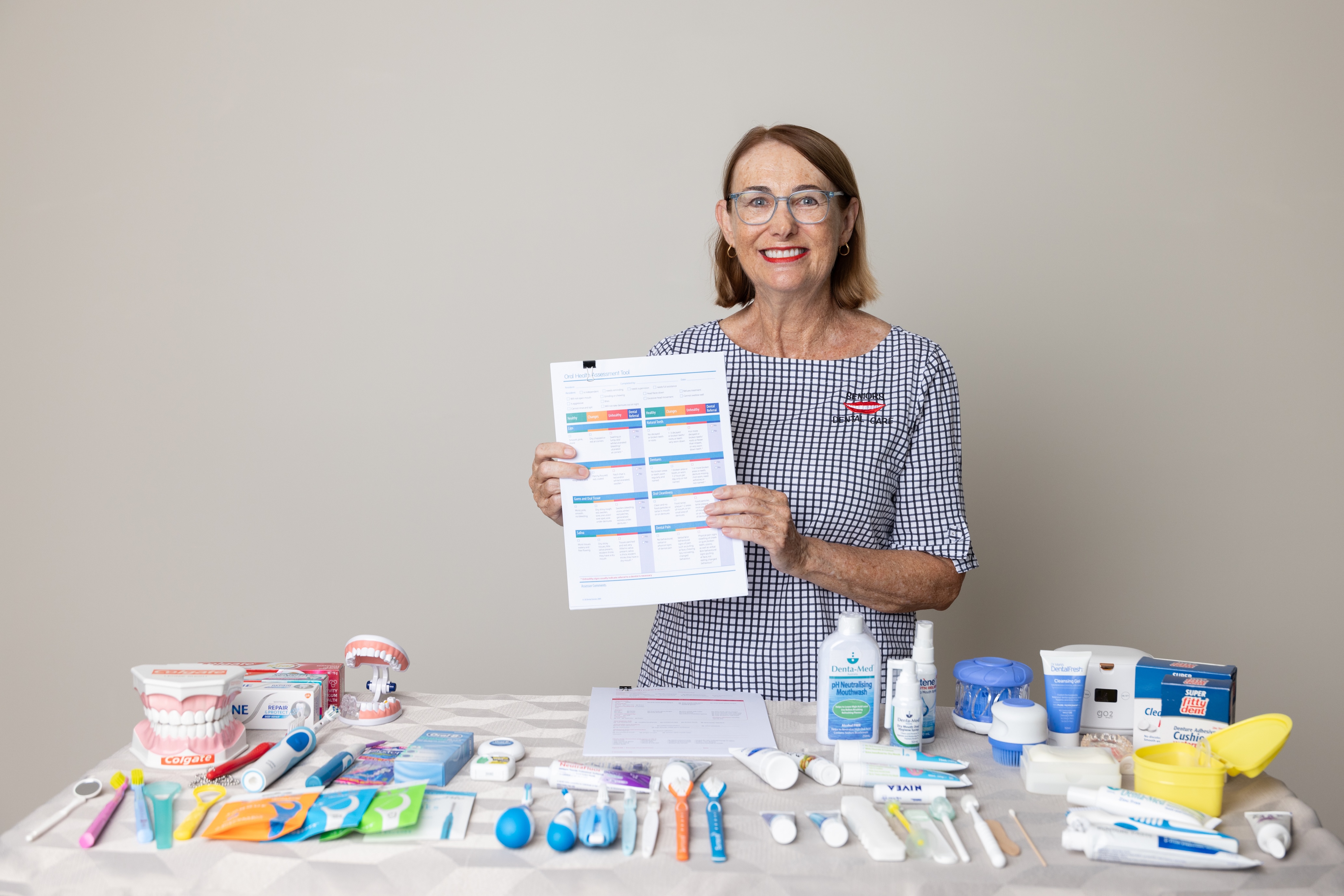 Woman stands behind a table of dental care products, holding an oral health information sheet.