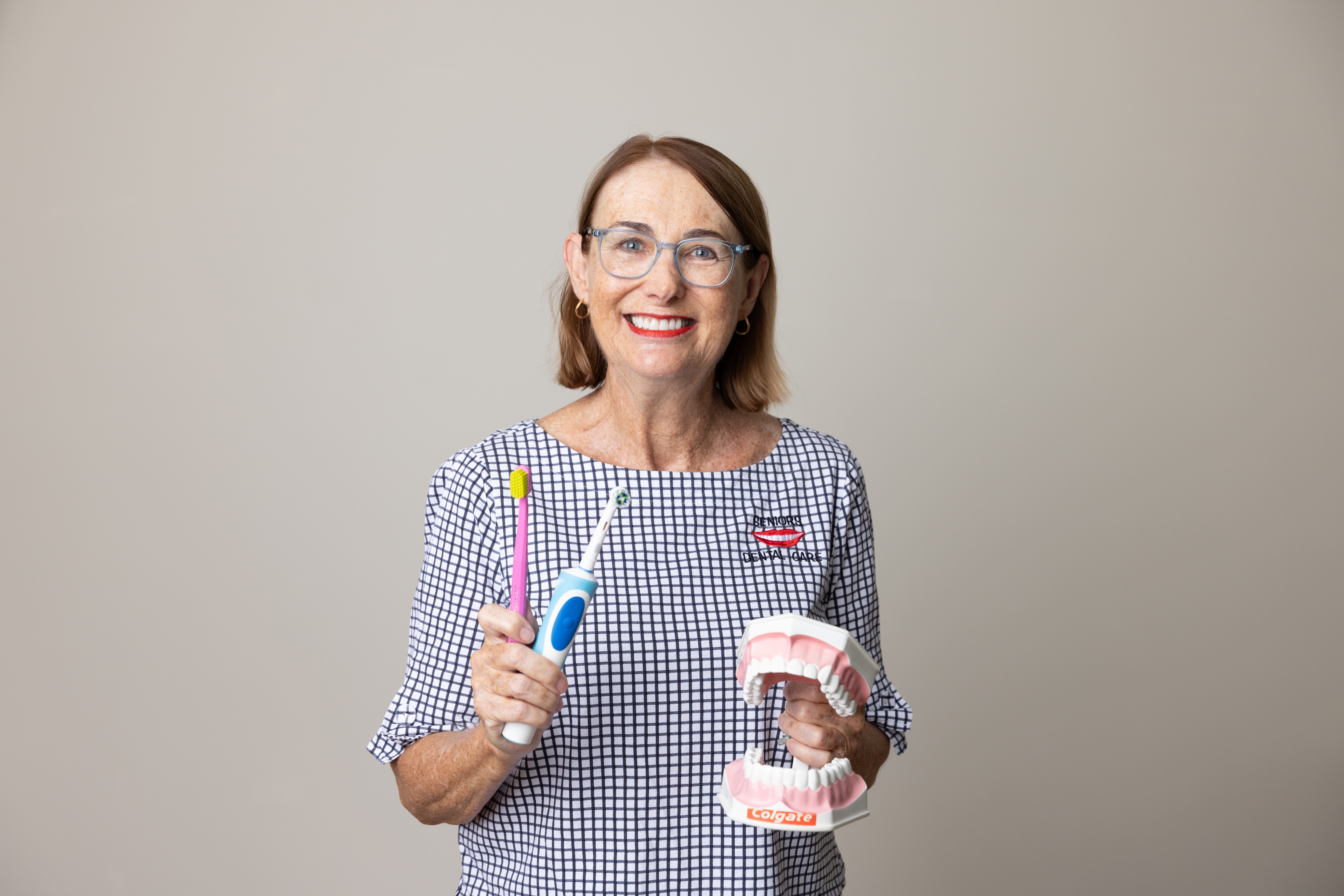 Smiling woman holds a toothbrush, electric toothbrush and a dental model to demonstrate oral care.