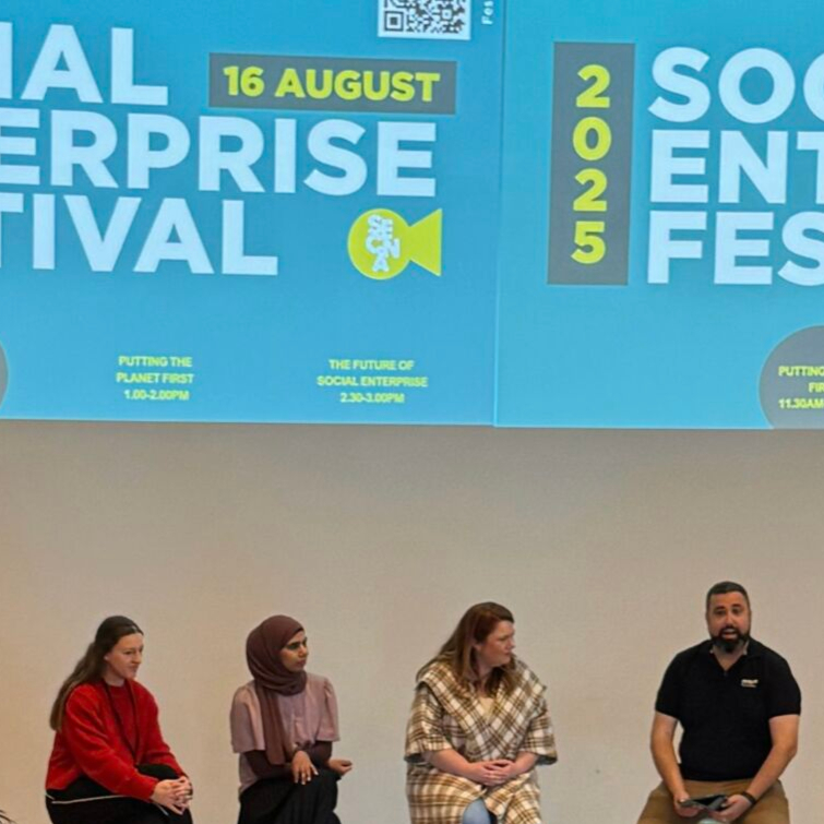Four speakers sit on stage under a large blue banner for the Social Enterprise Festival 2025, engaged in a panel discussion.
