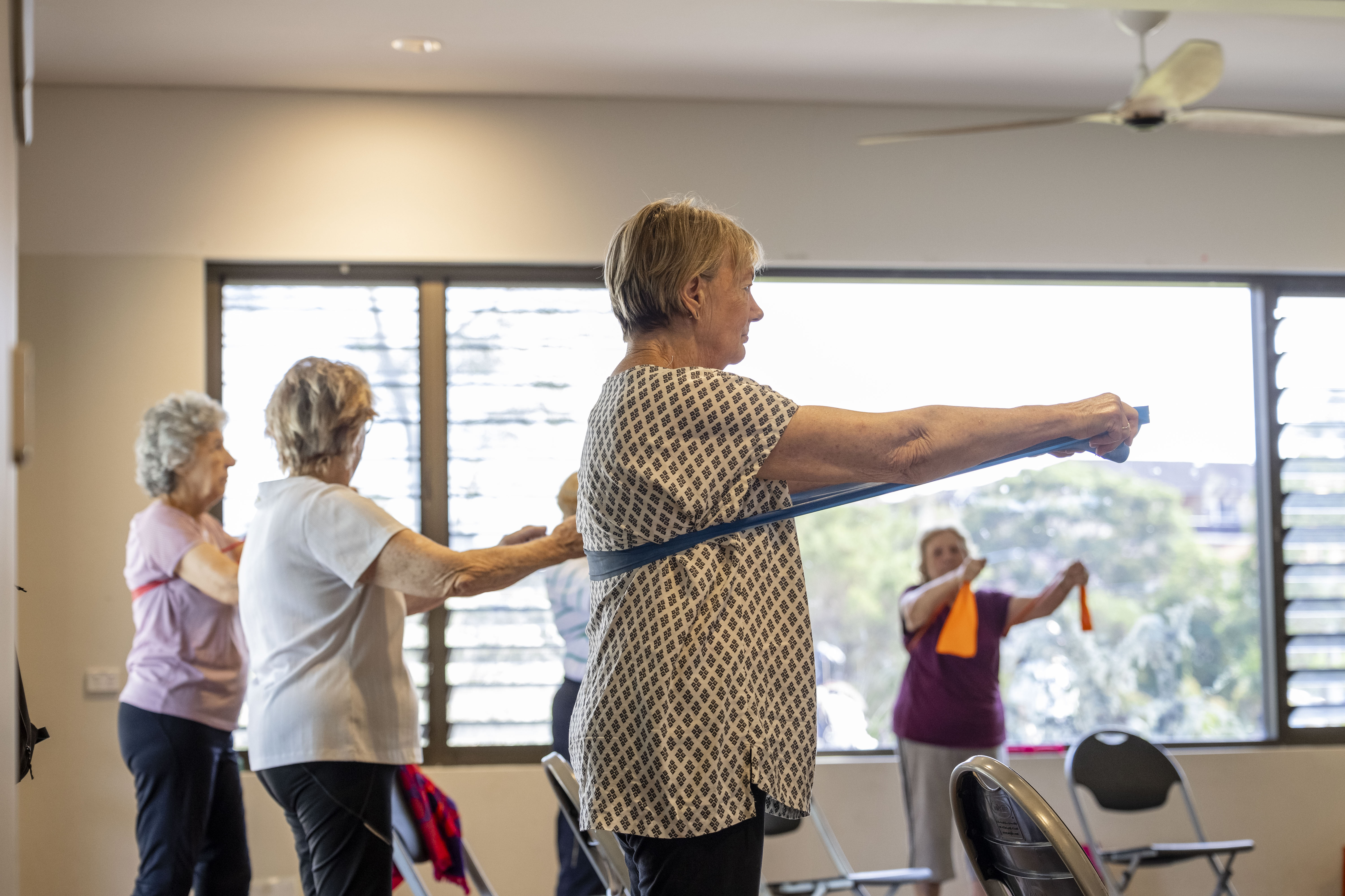Older adults use resistance bands during a gentle exercise class indoors.