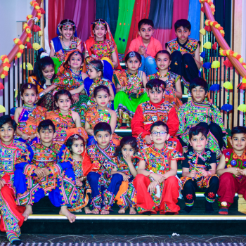 Children in colourful traditional Indian outfits dancing with sticks at an indoor event.