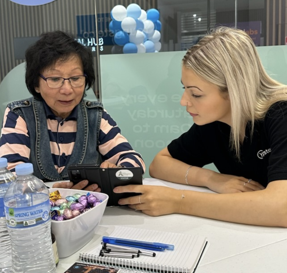 A Youngster.co volunteer helping an older woman navigate her smartphone at a digital skills drop-in session
