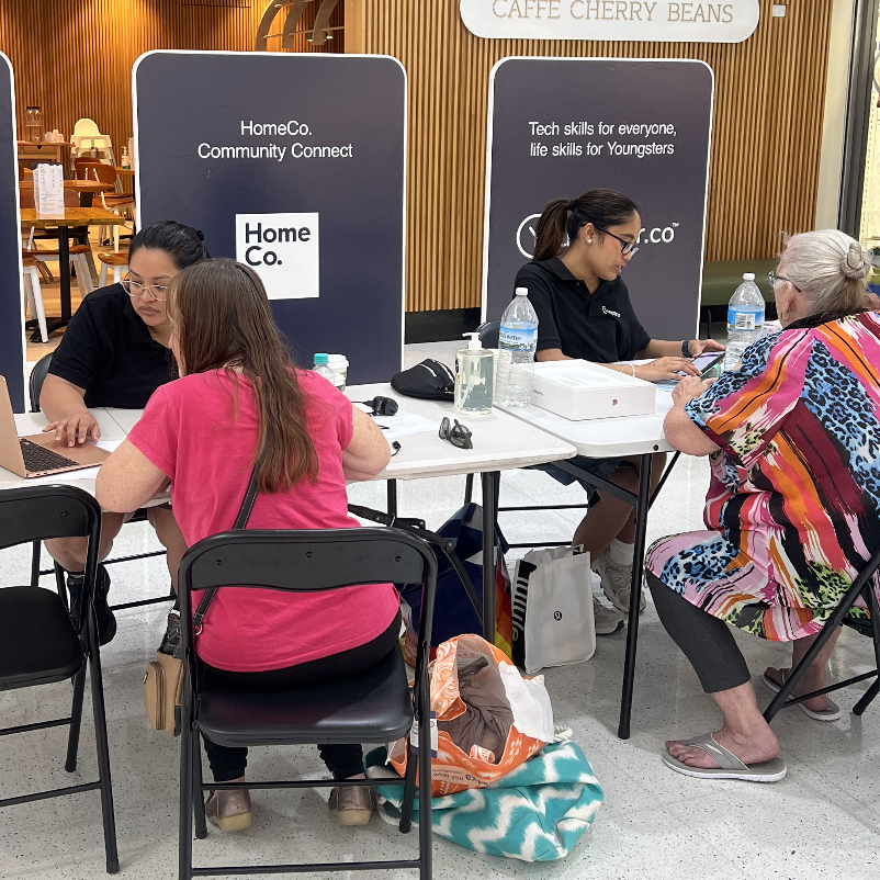 Two Youngster.co volunteers providing one-on-one digital skills assistance to community members at a HomeCo Community Connect pop-up in a shopping centre
